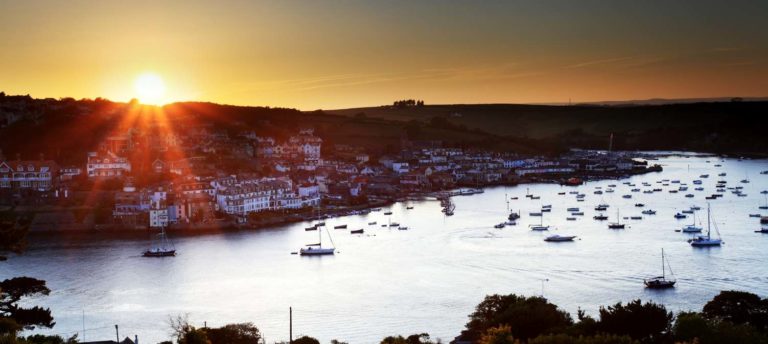 Salcombe coastline at sunset showing homes and boats moored in the sea